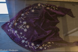 <center>Conflans : Musée d’Art et d’Histoire.</center> Châle edelweiss. Seconde moitié XIXe siècle. Tarentaise.
Des edelweiss, du châle...
Ce châle de velours triangulaire, de la seconde moitié du XIXe siècle, bordé à l'origine par de la dentelle ou des franges, était traditionnellement porté avec la coiffe appelée Frontière dans les cantons d'Aime et de Bourg-Saint-Maurice. Les broderies blanc-argent et la couleur, le violet, du châle font penser à la période de demi-deuil. Le costume, important marqueur social et culturel, connaît également des règles strictes liées à la perte d'un proche. Cette dernière est suivie d'une période de deuil puis d’une période de demi-deuil. Ces temps sont plus ou moins longs selon le degré de filiation, et peuvent varier selon les territoires. Il est donc difficile de faire une généralité pour la Savoie, mais à titre d'exemple nous pouvons admettre qu'une veuve porte le deuil un an et demi, suivi du demi-deuil de six mois (compter trois ans au total à Hauteluce par exemple) ; quand la perte d'une tante ou d'un oncle peut être signifiée par six mois de demi- deuil.
En général, le grand deuil impose le noir et des matières comme le lainage. Le demi-deuil autorise le violet, le mauve, le bleu, le gris et le velours ou le taffetas.
Le décor ne semble pas régi par des règles aussi strictes que la couleur ou la matière. Les fleurs brodées en gris-argent doivent être liées à un goût personnel.