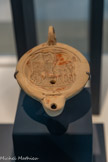 <center>MuséAl</center>Lampe à huile.
Tterre cuite.
 2e moitié du premier siècle..
 Alba / Forum. <br>
L'attelage transportait les images des divinités lors des cérémonies religieuses,  ou servait de voiture d'apparat. Ce type de char a pu circuler sur la voie sacrée, entre le sanctuaire du centre-ville et celui de Bagnols. <br>
La plupart des lampes à huile retrouvées sont en terre cuite. Elles proviennent d'Italie ou d’ateliers régionaux. A Alba, beaucoup de ces lampes ont été retrouvés à la nécropole Saint-Martin.