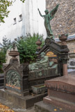 <center>Le cimetière du Montparnasse. </center> Charles Pigeon, 1838 - 1915, est un inventeur et entrepreneur français. Il fut le premier à produire et commercialiser un appareil d'éclairage portatif à essence breveté, ininflammable et inexplosible, reconnaissable par le dessin d'un pigeon posé sur un globe terrestre tenant en son bec une lampe. Charles Pigeon est enterré avec sa femme (décédée en 1909) dans une tombe de marbre particulièrement originale : les deux époux y sont représentés en tenue de ville (manteau pour l'un, robe élégante et coiffe pour l'autre), sur un lit à colonnades. Elle est étendue et lui à demi-allongé à sa gauche, tourné vers elle en appui sur un coude, comme s'il lui faisait la lecture du livre qu'il tient de la main gauche. Au-dessus du lit, un ange veille sur eux.