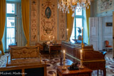 <center>Grand cabinet </center>Canapé.  Georges Jacob. 1765-1799. Canapé en bois doré sculpté reposant sur six pieds toupies cannelés et rudentés. La traverse supérieure du dossier, ornée de deux pommes de pin, la ceinture et le dessus des accotoirs sont sculptés de chutes de piastres, tandis que les montants verticaux sont ornés d'un filet de doubles perles et de culots de feuilles de refend. Les dés de raccordement sont ornés de quatrefeuilles. Le canapé est garni d'une tapisserie à fond blanc cassé, comportant sur le dossier un motif de draperie bleue à franges d'or ornée de fleurettes blanches, s'ouvrant au centre sur un bouquet émergeant d'un vase en forme de trompette et comportant à gauche une tulipe perroquet, dans un encadrement de branches de buis. La composition centrale est flanquée de couples de colombes