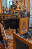 <center>Grand cabinet </center>Ecran de cheminée. Ecran rectangulaire à double face, monté sur patins cannelés et terminés par des cubes cannelés. A la partie supérieure au point d'intersection des montants moulurés : rosaces sculptées sur trois faces. Au milieu vase en saillie à double face avec guirlande de feuillage retombante. Il est garni, d'un côté, d'une tapisserie au point figurant une danseuse antique en grisaille sur fond rouge dans un encadrement de feuilles également en grisaille et, de l'autre côté une soie rose brochée de guirlandes roses en rivière separées par des bandes verticales portant un décor analogue plus petit. <br> Pendule aux enfants musiciens. 1780. Sur un socle en marbre griotte rouge et bronze doré, orné de têtes de Méduse dans un médaillon, de sphinges et de rinceaux, prennent place trois figures en bronze patiné. Au centre, le cadran émaillé blanc est surmonté d'un putto jouant des cymbales. De chaque côté du cadran, lui-même posé sur une base en bronze doré orné d'une scène d'offrance à l'antique en bas-relief, sont assis deux enfants faunes jouant de la trompe. Des instruments sont disposés à leurs pieds.