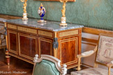 <center>Chambre d'apparat de Mme Thierry de Ville d'Avray.</center>Commode. Guillaume Beneman, Pierre-Philippe Thomiren. 1787. Commode à trois vantaux en acajou et bronze doré à dessus de marbre bleu turquin. La façade se compose de trois panneaux dont la partie centrale est en léger ressaut. Le placage d’acajou est simplement souligné par des baguettes de bronze doré. La ceinture est ornée d’une frise de canaux et de pointes d’asperge qui dissimulent trois tiroirs. La commode repose sur quatre pieds toupies cannelés supportent les montants agrémentées de figures féminines canéphores en gaine. Cette commode fut commandée par Marc-Antoine Thierry de Ville d’Avray en 1787 pour la chambre de son épouse, dans son appartement situé au sein du Garde-Meuble. Guillaume Beneman ou Benneman (vers 1750-vers 1811), reçu maître ébéniste le 3 septembre 1785, connait très vite le succès et succède à Riesener comme fournisseur de la Couronne. Ces productions se caractérisent par une élégance raffinée et des formes pleines, assez massives et bien proportionnées. <br> Pendule aux dauphins.  Charles Le Guay, Manufacture de porcelaine de Sèvres. 1781. Pendule en forme de vase balustre comportant des anses en forme de dauphins. La porcelaine est en bleu sombre. Elle est complétée d'un décor doré entourant le cadran. Les dauphins sont en porcelaine blanche et dorée. Des motifs de glaçons dorés surmontent la pendule et sont rejoints par les têtes des dauphins. Cette pendule est une réédition d'un modèle créé en 1775 à Sèvres et acheté en 1777 par Louis XVI pour le cabinet des bains du château de Versailles.
