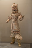<center>Musée Cernuschi. </center> Gardien de tombe.  206. Terre cuite, Moulage, Polychromie. Statuette, Mingqi. Cet impressionnant personnage courroucé, au visage particulièrement expressif, à la pose véhémente, tenait autrefois un glaive de la main droite. On notera la présence d'éléments fortement en saillie, telles les cornes qui ornent les épaulières et les sourcils broussailleux du personnage.