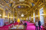 <center>LA SALLE DES CONFERENCES </center> Faisant face à la Cour d’honneur, dont elle prend le jour par neuf fenêtres, cette salle imposante présente un décor largement rehaussé d’or, composé d’allégories à la gloire de Napoléon Ier et de l’histoire de France. Elle abritait, dans sa partie centrale, le trône impérial, appuyé contre la paroi méridionale, sous un baldaquin porté par des cariatides. Pour cette raison, on lui donna d’abord le nom de « salle du Trône ». La salle des Conférences est coiffée d’une voûte qui se développe de part et d’autre d’une coupole sur pendentifs. La structure des deux portions de la voûte, délimitées par des arcs doubleaux, est particulièrement complexe. Des compartiments à bordure sculptée et dorée délimitent les peintures à sujets historiques et les médaillons à profil antique, qui ornent le sommet de chaque portion. Autour de la table de lecture, les sièges historiques du Sénat conservateur sous le Consulat.