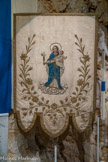 <center>Le musée.</center>Une bannière de procession ornée d'une Vierge en pied, en tissus appliqués (velours, sois, lamé d'argent) et rebrodés de soies polychromes, paillettes, filés et lames d'or. Elle est agrémentée de peinture sur toile (visages, mains et pieds).