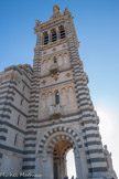 <center>Notre-Dame de la Garde</center>D'une hauteur de 41 mètres, le puissant clocher carré situé au-dessus du porche d'entrée comporte deux étages identiques formés de cinq arcatures, celle du milieu servant de fenêtre à un petit balcon. Cet ensemble est surmonté d'un beffroi dont chaque face est constituée de trois grandes baies aux colonnes de granit rouge derrière lesquelles sont placés les abat-sons.