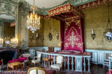 <center>Le château de Champs-sur-Marne. </center>Chambre d'honneur aménagée comme une  chambre d'apparat du 18 ème siècle. À l’origine chambre usuelle, cette pièce est décorée en 1740 par le second duc de la Vallière dans le style rocaille, en vogue sous le règne de Louis XV ; l’auteur des boiseries reste encore mystérieux. Mais les colombes sculptées, les queues de paons, les frises de bois qui s’enroulent autour des miroirs font de cette pièce un véritable décor de théâtre amoureux qui n’est pas sans rappeler la passion du duc de la Vallière pour le théâtre. Au XIXe siècle, la pièce sert de chambre d’enfant. Lorsque les Cahen d’Anvers s’installent, ils font de cette chambre une chambre d’honneur, comme le veut l’usage dans certains châteaux. Ils remettent un tissu du XVIIIe siècle dans l’alcôve. Ils ajoutent une balustrade acquise dans un château bourguignon. Ils font construire un lit à la duchesse, recouvert de damas rouge avec des applications de galons jaune et blanc. Cette mise en scène d’un XVIIIe siècle fantasmé permet de transformer cette chambre en véritable chambre royale. Devant la cheminée, on peut voir une duchesse brisée. À gauche du lit, un bonheur du jour de Charles Topino est décoré d’une marqueterie de tasses, soucoupes, vases et fleurs.