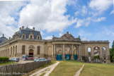 <center>Chantilly. Les grandes écuries. </center> Entrée des Grandes Écuries par un des pavillons (gauche) et manège extérieur (droite). Sous la direction de Rémy-François Bridault, l'ensemble fut orné, de 1733 à 1736, de sculptures vigoureuses magnifiant des chevaux impétueux au-dessus des portes du pavillon central et des pavillons carrés. Les trois chevaux hennissants sont sculptés en faible relief et présentés de profil dans des positions différentes.