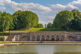 <center>Canal de la Poêle. </center>La Grotte, située au-delà du Grand Canal est due à Le Nôtre qui l’a conçue, et à Le Brun qui a dessiné les sculptures. Les grottes sont appréciées depuis la Renaissance.
À Vaux-le-Vicomte, son originalité tient au fait que sa façade présente une surface plane, alors que traditionnellement elle a une forme de caverne. Elle présente des éléments traditionnels comme le bossage et les termes, mais ces caractères sont tempérés par leur adaptation au terrain. Elle est flanquée par les statues de 2 Dieux-fleuve : Le Tibre (à gauche) et l'Anqueuil (à droite). Huit Atlantes encadrent 7 niches comportent des rochers artificiels. Vue de loin la grotte semble faite en pierres à peine travaillée, et les niches ont l’air d’abriter des sculptures très travaillées. Mais de près, c’est le contraire. La Grotte est encadrée d’escaliers, de rampes et de terrasses.
