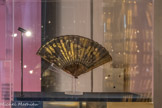 <center>Sous l’ombrelle</center>Eventail de type plié Vers 1820
Feuille en soie brodée de paillettes dorées Tête des personnages en ivoire Monture en bois, panaches en corne incrustées de paillettes
Collection particulière