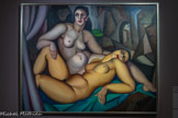 <center>Tamara de Lempicka (1898 -1980)</center>Perspective ou Les deux amies 1923.
Huile sur toile. <br>
Tamara de Lempicka, exilée depuis Saint- Petersbourg, a développé au sein de l'Académie Ranson puis de l'Académie de la Grande Chaumière un style à la croisée du maniérisme de la Renaissance et du néocubisme, et fléchissant vers la mode Art déco de son époque. Cette œuvre qui mêle rigueur cubiste et sensualité des formes, est remarquée dès son exposition au Salon d'automne de 1923.
I e tableau révèle un moment de forte intimité érotique entre deux femmes. Lempicka,