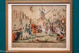 <center>« Marche du Dom Quichotte moderne pour la deffence du Moulin des Abus »</center>Anonyme.
France, après 1791.
Gravure en taille-douce, imprimée sur papier vergé et colorée à la main.
Mucem, Marseille. <br>
Le genre de la caricature politique s'affirme au 18e siècle. Ridicule, don Quichotte y est souvent représenté. Cette gravure cible les « Émigrés », qui ont fui la Révolution française et formé une armée contre- révolutionnaire derrière le prince de Condé en 1791. Parmi d’autres figures grotesques, on reconnaît les portraits à charge de « Sancho Tonneau dit Mirabeau » et du « petit Condé » en don Quichotte moderne. Tous défilent pour défendre le « moulin des abus », au toit surmonté de la tête de Louis XVI, « l’accapareur ».
On y retrouve aussi la Folle, avec ses grelots et sa marotte : voyez-vous comment elle s’ingénie à mettre en mouvement les pales du moulin ?