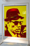 <center></center>Bernard RANCILLAC
1931, Paris (France)
2021, Malakoff (France)
Malcolm X
1968
Sérigraphie couleur sur double plexiglas, portant métallique
Inv. c.72.2.26 Achat 1972.
Bernard Rancillac s'affirme comme un peintre, préoccupé par la question de l'engagement et de l'image. Nourri de la grande peinture réaliste française du XIXe siècle et de la bande dessinée, il est à ses débuts très proche de Peter Saul et de l'univers du jazz. Il travaille à partir d'images agrandies à l'épiscope et peintes en aplats de couleurs franches et très contrastées.
En 1968, Il réalise des portraits emblématiques de l'Amérique contestataire, dont celui de Malcolm X, le leader noir assassiné. Il s'agit d'un multiple où se manifeste la dialectique peinture-photographie et peinture-sculpture. Une photographie noir et blanc, image de presse ou de télévision, est sérigraphiée sur deux plaques de plexiglas. Là, se détache le visage, bleu d'un côté, rouge de l'autre, dans son espace jaune (évoquant l'or des icônes). Le cadrage renvoie à l'instantané (chapeau coupé, bouche ouverte laissant entendre qu'il est en train de parier). Le spectateur rencontre l'œuvre dans l'espace, elle n'a ni recto ni verso, ni dans sa surface, ni dans son volume. C'est une image surdimensionnée, vacillante, suspendue à un portique blanc autour duquel on peut circuler.
« À l'origine de toute création artistique, il faut une émotion. Très souvent chez moi, elle est de nature politique, même quand je peins des Mickey, des musiciens de jazz, des voitures ou des stars de cinéma. »