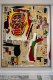 <center></center>Jean-Michel BASQUIAT
I960 -1988, New York (États-Unis)
King of the Zulus
1984-1985
Acrylique sur toile, pastels gras et photocopies sur papiers contrecollés
Inv. C. 86.39 Achat, 1986.
Enfant de la classe moyenne, Jean-Michel Basquiat est très tôt encouragé par ses parents à cultiver sa fibre artistique. Il acquiert une visibilité sur la scène new-yorkaise fin 1978. Dans un contexte où le tag et le graffiti sont devenus un phénomène urbain et avec eux le hip hop, Basquiat opère une synthèse entre l'expression codée des gangs et les souvenirs de ses visites de musées. En 1980, il se lie d'amitié avec Andy Warhol avec lequel il réalisera plusieurs toiles entre 1983 et 1985. La fulgurante reconnaissance de Basquiat coïncide avec l'émergence du Bad Painting aux États-Unis et de la Figuration Libre en France.
King of the Zulus [Le roi des Zoulous] est tout d'abord le titre d'un morceau de Louis Amstrong. S'il pointe un ailleurs exotique, son primitivisme est l'écho contemporain de la Nation Zulu, branche non violente du Hip Hop. Peintre de la mégalopole, Basquiat transpose au tableau la technique instrumentale de l'échantillonnage, combinant des fragments de mots, d'images et de symboles comme autant de samples visuels. Le recours à la photocopie couleur - procédé alors nouveau - lui permet d'opérer des reprises de dessins antérieurs et d'inscriptions empruntées à différents champs du savoir. Ce réseau de signes éclectiques et de motifs récurrents, constitue le fond d'où se détache la figure humaine, thème central dans son œuvre, indissociable pour lui de l'environnement social et culturel, orchestré par la toute puissance de l’information.