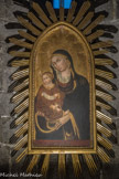 L'église San Donato. La mère et l'enfant sont presque frontaux et regardent vers le spectateur. Marie tient l'enfant Jésus de la main droite, tandis que de la gauche elle l'enveloppe dans son manteau. L'enfant tient un parchemin dans la main gauche, tandis que la droite tient son pied gauche. Le goût de la ligne ressort, un des éléments caractéristiques de la peinture siennoise, comme en témoigne le rythme sinueux et presque calligraphique du bord doré du manteau de la Vierge, des voiles blanc et violet, la finesse des formes des personnages qui se détachent sur le fond doré. L'exubérance décorative se remarque également dans l'anneau de Marie, dans le pendentif en corail au cou de Jésus, dans les broderies dorées à fleurs et feuilles typiques du gothique tardif, sur les vêtements de l'Enfant, dans les décorations perforées qui ornent les bords des vêtements, les auréoles, les bords de la table en bois se terminant par une cuspide divisée en cinq lobes.