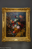 <center>Fleurs.</center>Jean-Baptiste Monnoyer.
Lille, 1634 ou 1636-Londres, 1699.
Huile sur toile.
Formé à Anvers» Monnoyer se rend à Paris où il collabore avec Charles Le Brun et Pierre Mignard. Spécialiste de la nature morte, de fleurs et de fruits, il travaille pour les manufactures des Gobelins ou de Beauvais, mais aussi pour les maisons royales, et notamment à partir de 1678 pour la décoration des grands salons de Versailles.
Ce tableau est caractéristique de son art.
On y retrouve le répertoire commun à un grand nombre de ses compositions : le tapis frangé d’or, la tablette de marbre, le vase en vermeil ou en bronze doré dans lequel prend place un flamboyant bouquet de fleurs. Monnoyer comme à son habitude décrit avec une minutie et réalisme les diverses espèces florales, simples fleurs des champs ou espèces rares et coûteuses de son temps, le tout savamment composé pour évoquer le luxe versaillais.