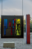 <center>La Cité Radieuse.</center> Vitrail incrusté dans la grande fenêtre carrée de 2,26 m du hall. Dehors, la stèle des mesures, sculpture géométrique, rouge et bleue, couleurs du Modulor, incrustée de nombres de cuivre de petite taille. Cette sculpture sera l'objet de l'admiration des artistes minimalistes américains.
