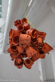 Sans titre
2001, plastique, corde polyamide
Comme tu as pu le remarquer, Anita Molinero aime suspendre ses œuvres au plafond et laisser ses sculptures se libérer du socle sur lequel on aimait les poser à l’époque classique.
Pour réaliser cette suspension, l’artiste a récupéré un stock de pots de fleurs en plastique. Elle les a chauffés, déformés, troués et assemblés en grappe, Le tout est suspendu à une corde comme attrapé dans le piège d’une toile d’araignée ou du filet d’un pêcheur.
Encore une œuvre un peu monstrueuse qui complète le défilé du freak show que tu peux admirer dans cette salle. Cependant, elle semble tirer sa monstruosité non seulement de sa déformation mais aussi de son piteux état et de son apparente fragilité. On dirait que les pots ont été abîmés par le temps et pourraient s'écrouler à nos pieds à tout moment.
Collection du fonds régional d’art contemporain Occitanie Montpellier, France.