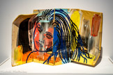 Ghada AMER
1963, Le Caire (Égypte)
La Géante
2017
Céramique grès cérame; porcelaine, barbotine, pigments.
Inv. 2023.4.1  Achat. 2023.
Ghada Amer agit sur les plaques en céramique à partir des trois principes clés du travail de l'argile: aplatir, rouler et pincer. Se rappelant les assiettes de Picasso et Matisse qu'elle admirait dans son enfance à Nice, elle utilise l'aspect fortuit que prennent les bords extérieurs dans le processus de roulage à la main. Surélevés, ils lui permettent d'obtenir une apparence tridimensionnelle, comme un récipient ou un coquillage. La surface est peinte avec une barbotine teintée. Ensuite, l'artiste dessine des personnages de son répertoire familier, des portraits en gros plan de pin-up, avec de l'argile colorée roulée et appliquée sur fa surface.
Ghada Amer recourt cependant dans son travail à des pratiques dites féminines utilisant notamment la broderie. Elle explore ainsi la construction, point par point, du rôle de la femme, de la sexualité et de l'amour dans les sociétés contemporaines.