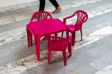Chapitre 2 : mobilier en plastique pour enfants le long de la lourde étagère administrative de 2 m de haut jusqu'à la petite table rose d'enfant en plastique fuchsia. Les rois du monde, Chapitre 2 : mobilier en plastique pour enfants