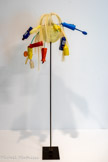 Martial RAYSSE
1936, Golfe-Juan (France)
Bird of Paradise
1960
Étudiant en lettres, Martial Raysse renonce à la littérature pour la peinture. À la fin des années 1950, il déploie une activité artistique dans plusieurs registres : poèmes-objets, lectures publiques, mobiles, masques, assemblages d'objets divers présentés dans des boîtes de plexiglas. À partir de sa rencontre avec Arman et Yves Klein, il devient l'un des fondateurs du Nouveau Réalisme Fasciné par la beauté brute du plastique, Raysse développe son concept d'hygiène de la vision qui met en jeu des objets de la nouvelle société consumériste. « J'ai voulu un monde neuf, aseptisé, pur et, au niveau des techniques utilisées, de plain-pied avec le monde moderne ». Après son séjour aux États-Unis, il se rapproche du Pop Art.
Bird of Paradise [oiseau de Paradis] est un assemblage d'objets monté sur une tige, métamorphosé par la profusion colorée des articles de séné qui le composent L'oiseau de paradis renvoie par associations sémantiques et plastiques à la parade, aux plumes, et par extension aux plumeaux, cuillères en plastique, à l'univers de la cuisine, du propre, du neuf, du balai, des flacons LUX (lumière). Ironiquement se tient à hauteur de regard une passoire, miroir ubuesque tendu au spectateur. Si l'oiseau de paradis de la réalité, à l'aigrette et aux plumes spectaculaires, est depuis toujours un spécimen fragile, Bird of Paradise est lui aussi affligé d'une fragilité spectaculaire : (Impossibilité de l'éternelle jeunesse.