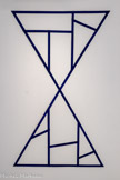 Daniel DEZEUZE
1942, Alès (France)
Sans titre
1975
Lamelles de bois agrafées et peintes
Inv. C.86.76 Achat, 1986
Daniel Dezeuze fait ses études à l'École des Beaux-Arts de Montpellier de 1959 à 1962. En 1970, il est membre-fondateur du groupe Supports/Surfaces, notamment avec Patrick Saytour et Claude Viallat Ensemble, ils posent la question du devenir de la peinture et de son rôle dans le paysage économique et culturel occidental. Ce groupe apparaît dans un contexte où ce n'est plus seulement le sujet de la peinture qui est remis en cause mais également ses éléments constitutifs : peintures et vernis, supports, méthodes et techniques de réalisation. Le groupe sera dissous en 1972 laissant une empreinte qui a contribué à de nouvelles approches artistiques.
La dénégation de l'illusionnisme pictural est pour Dezeuze l'occasion d'interroger le regard, ses conventions, ses rapports avec le réel et l'espace. Il opère par une série de déplacement de la peinture à la sculpture, de la sculpture au dessin.
Dezeuze s'attaque à la structure même du tableau et expose dès1967des châssis privés de leur toile, posés au sol. Sans titre s'inscrit dans cette dynamique. Grilles géométriques en latte de bois, quadrillages et triangulations, ces variations du châssis lui permettent de s'écarter des règles conventionnelles de la peinture. En adéquation avec la dissolution de la surface et du support, le pinceau est à son tour écarté au profit de gestes élémentaires : imprégnation, pliage, découpage, assemblage, collage, solarisation.