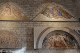 <center>Le Consistoire.</center>En bas, la Vierge assise à terre selon le type de la Madone d’Humilité est un motif en grande faveur dans la deuxième moitié du XIVe siècle. L’Enfant tient une banderole où est écrit EGO STJM LUX MUDI (Je suis la Lumière du Monde). Le commanditaire, le cardinal Jacopo Stefaneschi, est représenté agenouillé à droite de la Vierge.
En haut, le Christ ne tient plus de livre mais le globe du monde figurent les trois éléments : la mer, la terre et le ciel.
De sa main droite, il fait le geste de la Bénédiction.
Son visage n’est plus lisible à cause de la chute de l’enduit. De part et d’autres trois anges sont en adoration. Arc de l’intrados : orné de médaillons, rinceaux, feuilles d’acanthe. <br>
Le terme fresque vient de l’italien « a fresco » qui signifie « dans le frais ». Cette technique de peinture murale s’effectue sur un enduit qui est un mélangé de sable, d’eau et de chaux, avant qu’il ne sèche.
Au lieu de pénétrer dans le mortier, la couleur est prise dans le calcin, une pellicule dure et translucide qui se forme en surface au contact de l’oxygène.
L’exécution d’une fresque nécessite une grande maîtrise technique et beaucoup de rapidité. Voilà pourquoi elle est réservée aux grands maîtres.
