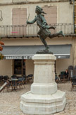 <center>Statue du Tambour d’Arcole et Rempart de Cadenet</center>Le bâtimets en arrière plan sont sur le tracé de l'ancien rempart. De 1545 jusqu’au 19e siècle, Cadenet était ceinturé par un rempart. Au fil du temps, le village s’agrandissant et le besoin de protection devenant inutile, les maisons se sont appuyées dessus. Le rempart disposait d’une série de tours qui défendaient quatre portes au total. Ici, le chemin de ronde dont il ne reste qu’un petit vestige, permettait d’accéder à la porte dite Sainte-Anne se situant entre les deux bâtiments, elle est actuellement matérialisée par les deux plots se trouvant au sol.