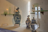 <center>Château de Lourmarin</center>La salle à manger. Les meurtrières, aujourd’hui,  servent de vitrines. Au centre, des faïence de Delft, entourées de verres de Murano (16ème-17ème s). Vaisselle d'usage en faïence blanche et bleue et au glacis brillant. Le décor central du vase représente une scène galante avec 2 personnages habillés à la mode du 18e siècle.
